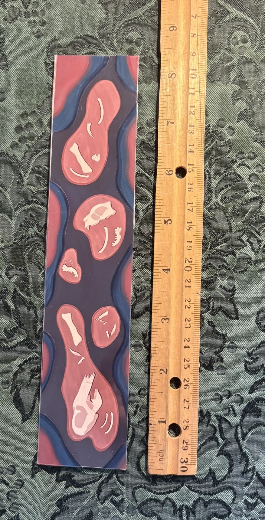 A glossy bookmark depicting a river of tar. A few pits in the tar reveal bones from prehistoric animals.