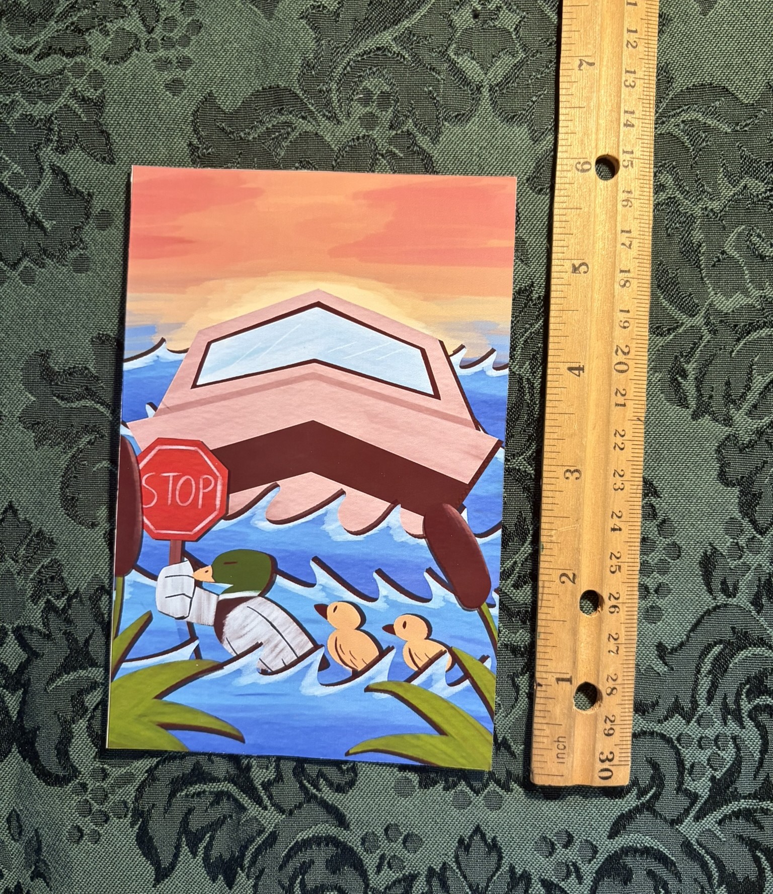 A 4 by 6 inch, glossy poster print. It shows three ducks crossing a lake, one holds a stop sign in its hand. Behind the sign is a boat waiting for the ducks to pass.